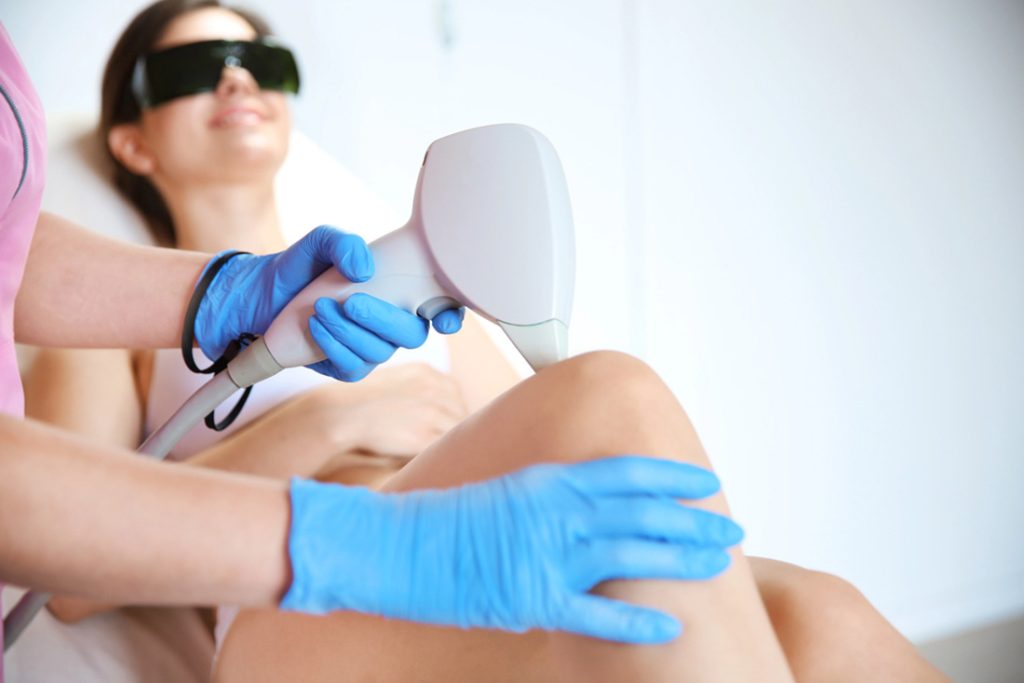 Certified technician performing laser hair removal on client's knee using protective eyewear for laser safety certification standards