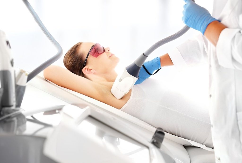 Professional performing underarm laser hair removal on a relaxed female client wearing protective eyewear in a modern clinic setting for medical aesthetics laser training.