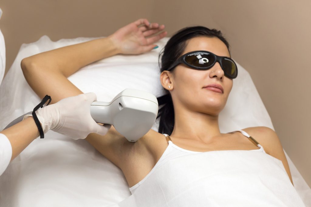 Student at a laser hair removal academy performing a precise underarm laser treatment on a client wearing eye protection.