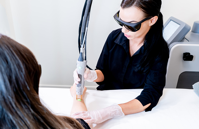 A professional technician performing a clinical procedure during laser hair removal training in woodlands to demonstrate proper handpiece technique on a patient's arm.
